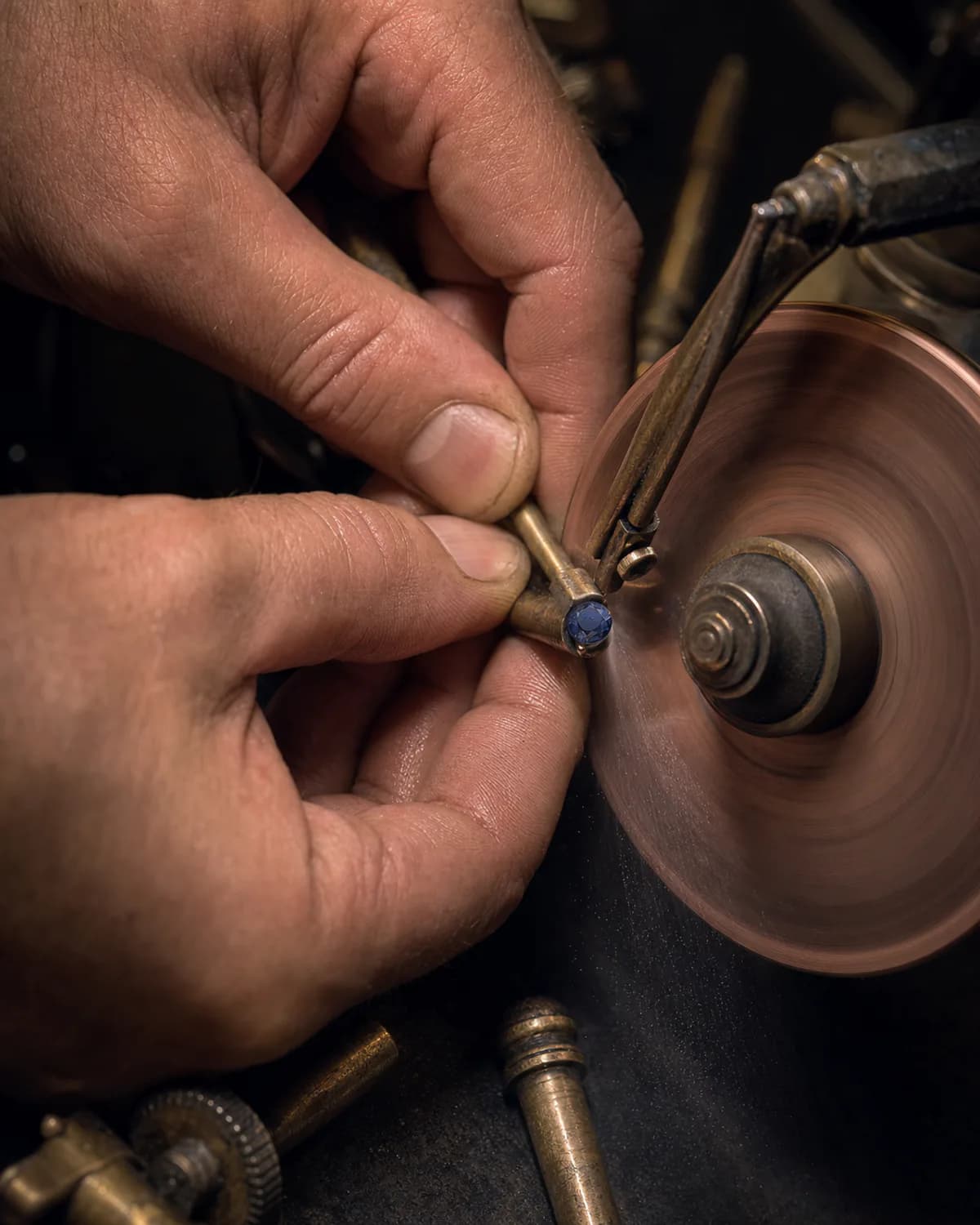 A lapidary faceting a blue sapphire on a polishing wheel