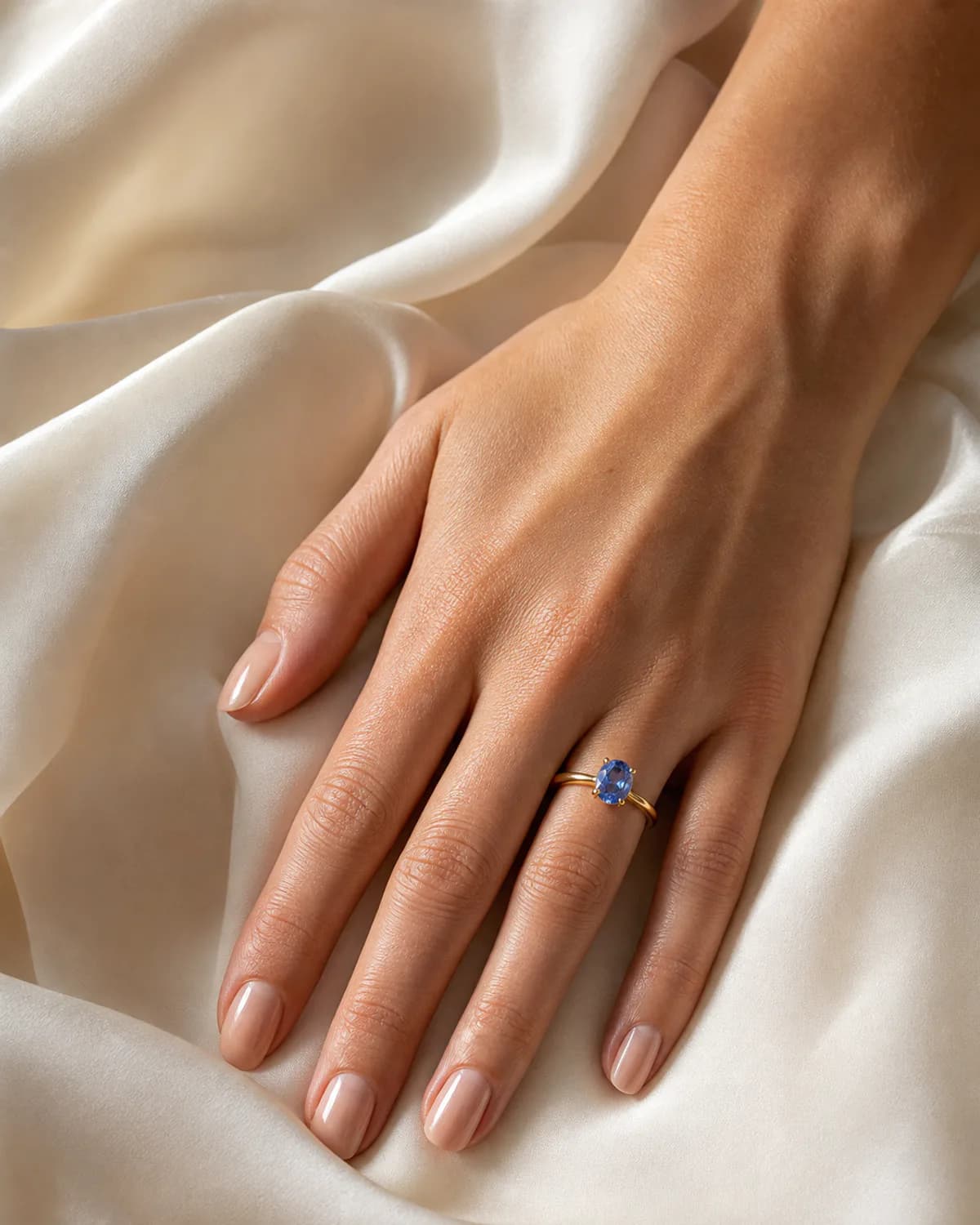 A Ceylon blue sapphire ring worn on an elegant hand against ivory silk